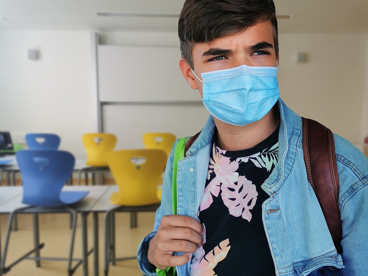 Das Bild zeigt einen Schüler, der eine medizinische Maske trägt, im leeren Klassenraum