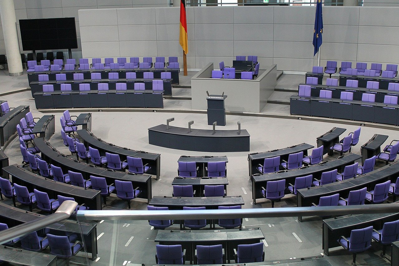 Das Bild zeigt die leeren blauen Sitze des Plenarsaals mit Blick auf das Sprecherpult