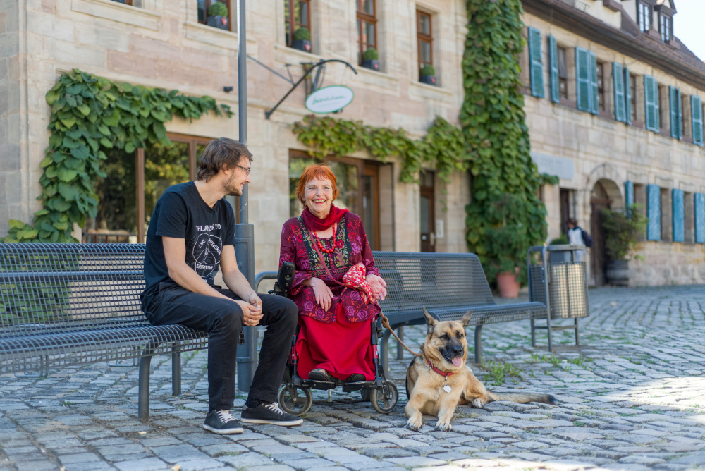 Foto von einem jungen Mann und einer Frau im Rollstuhl mit Hund in der Innenstadt
