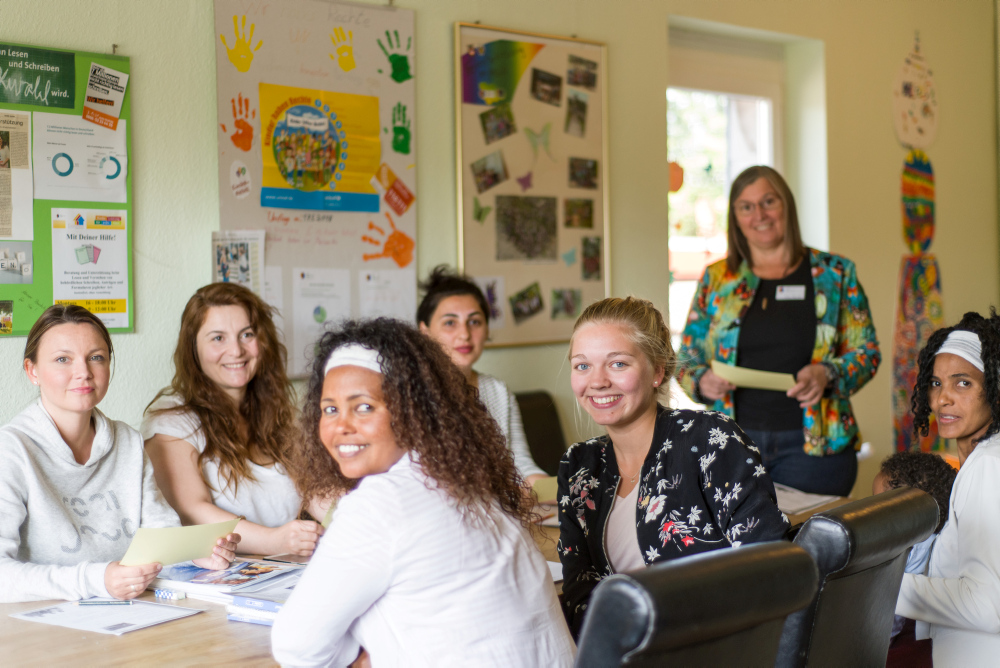 Foto von einre Gruppe Migranten, die zusammen mit einer Nachhilfelehrerin Deutsch lernen